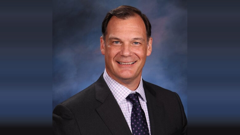 Smiling man in a suit and tie posed against a blue studio backdrop.