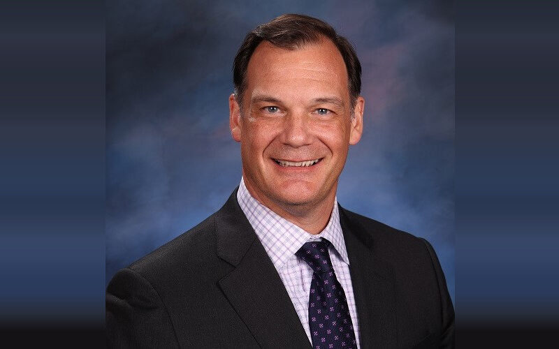 Smiling man in a suit and tie posed against a blue studio backdrop.