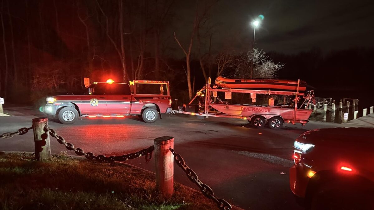 Emergency vehicles with flashing lights stopped on a dark road beside a trailer at night.