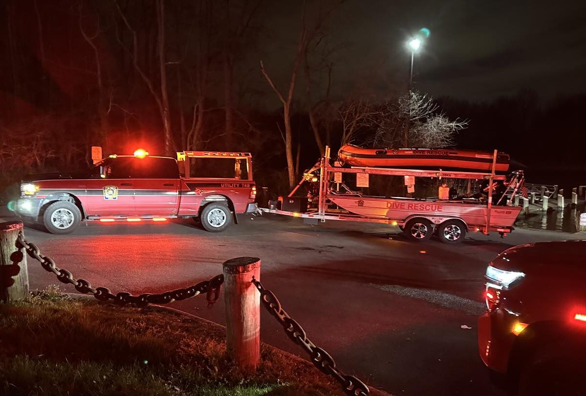 Emergency vehicles with flashing lights stopped on a dark road beside a trailer at night.