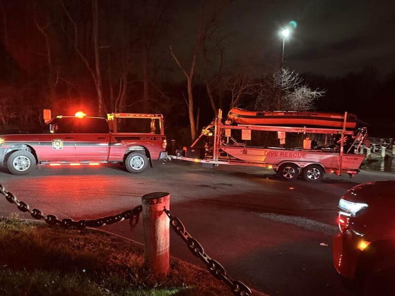 Emergency vehicles with flashing lights stopped on a dark road beside a trailer at night.