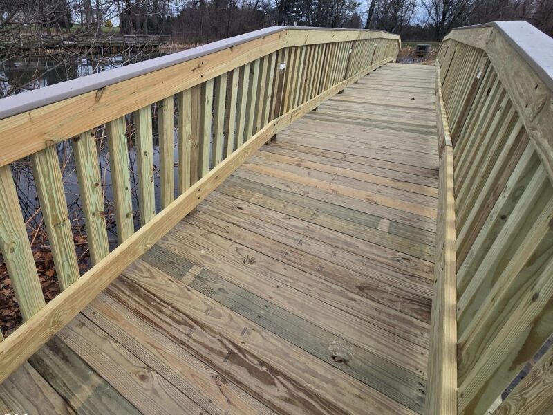 Wooden pedestrian bridge with railings over a wooded area on an overcast day.