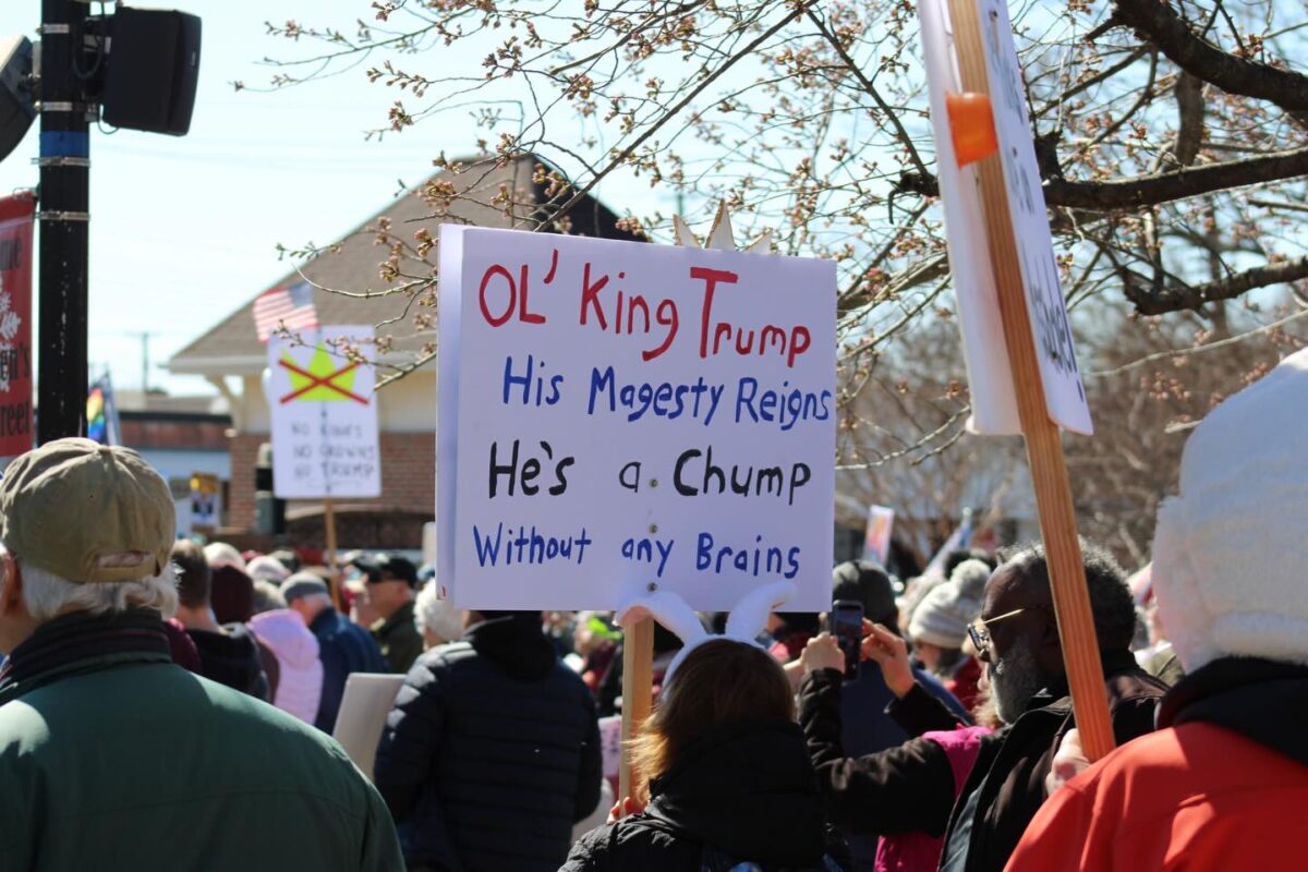Crowd at a protest holding a sign that reads "Ol' King Trump" and "He's a Chump Without any Brains".