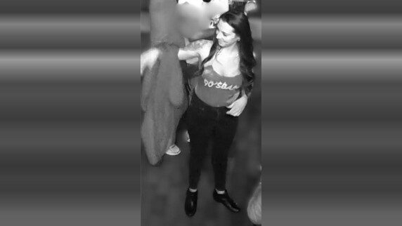 Black-and-white candid of a smiling woman standing indoors with other people nearby.