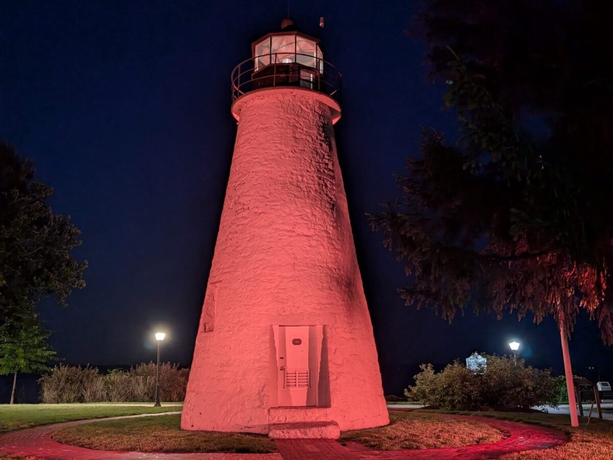 Pink-lit lighthouse at night with trees and a dark blue sky