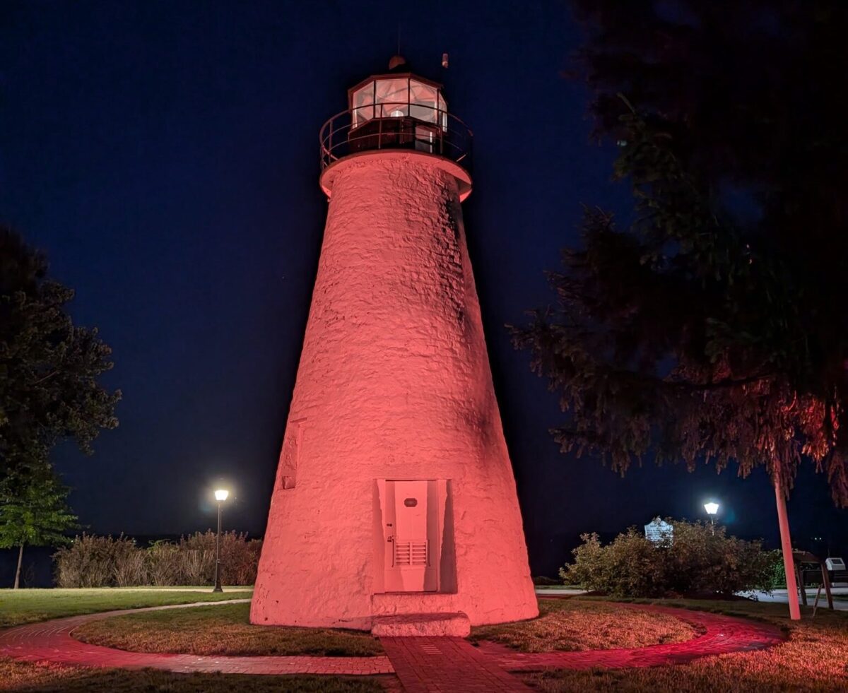 Pink-lit lighthouse at night with trees and a dark blue sky
