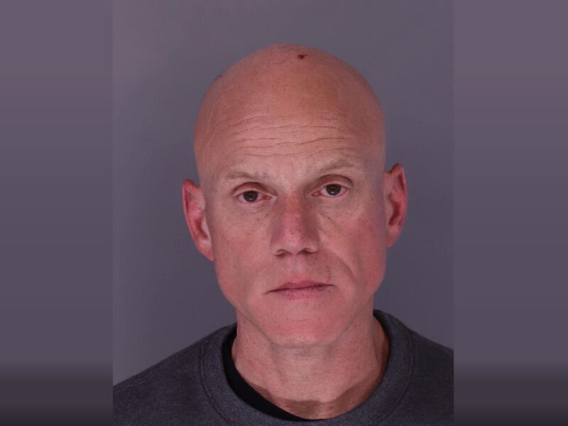 Head-and-shoulders portrait of a bald man against a plain gray background.