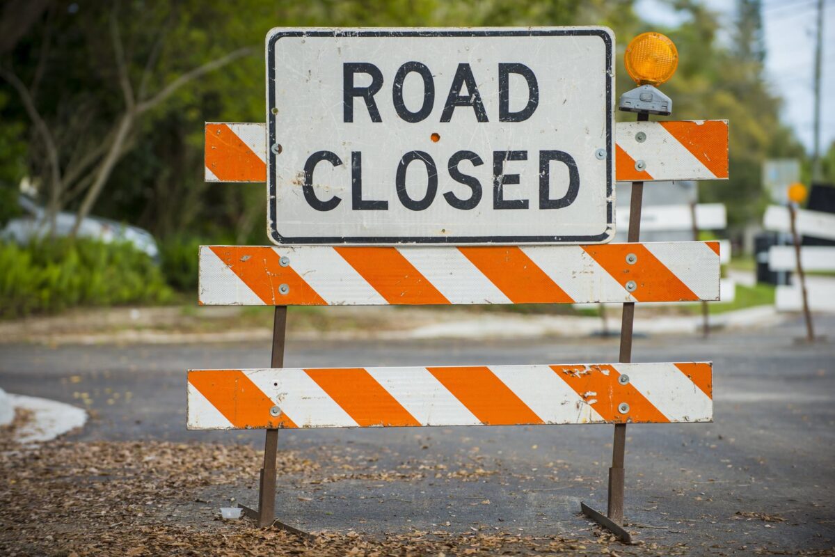 Road closed sign with orange-and-white barricades blocking a street
