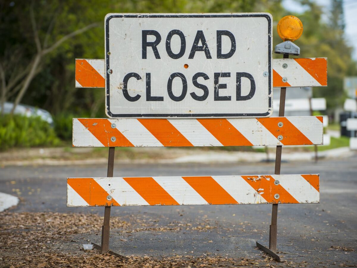 Road closed sign with orange-and-white barricades blocking a street