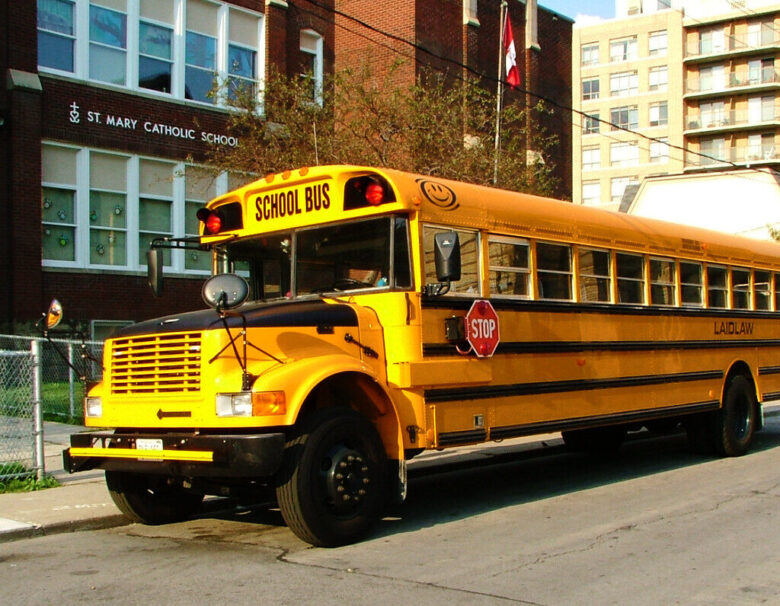 Yellow school bus parked beside a Catholic school building on a city street.
