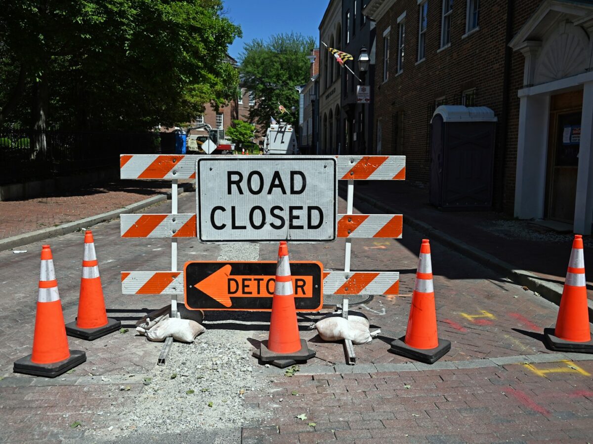 A road closed sign surrounded by orange traffic cones