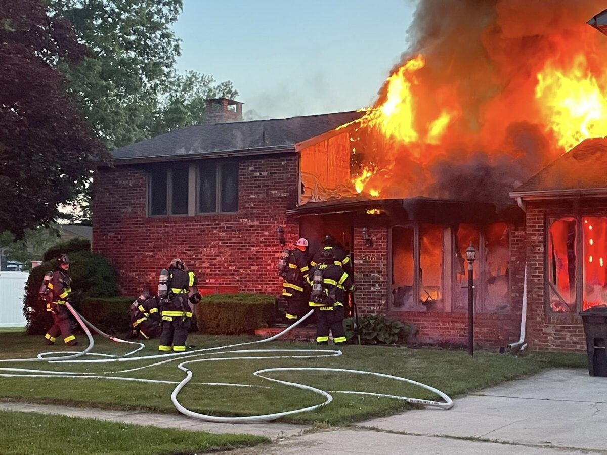 Firefighters battle a house blaze as flames engulf the front roof and windows.