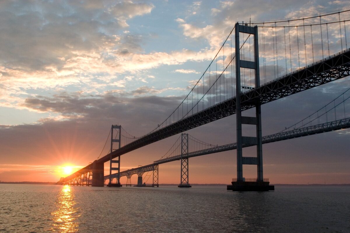 Suspension bridge at sunset over calm water with glowing sky and reflections