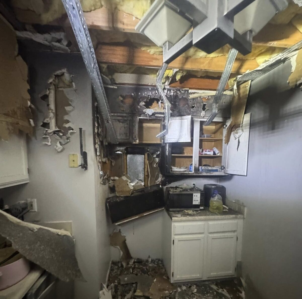 Severely fire-damaged kitchen with charred cabinets, debris, and exposed ceiling beams.