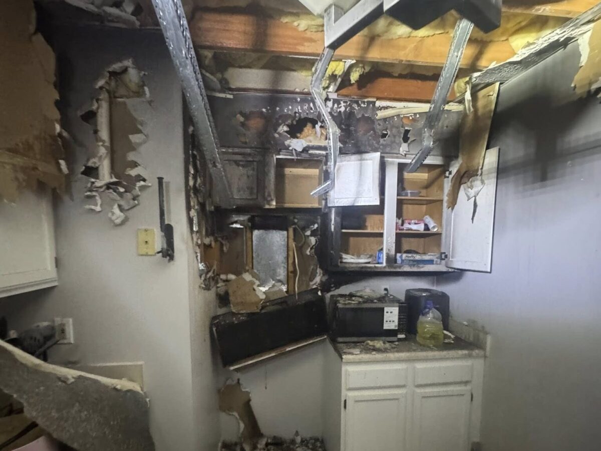Severely fire-damaged kitchen with charred cabinets, debris, and exposed ceiling beams.