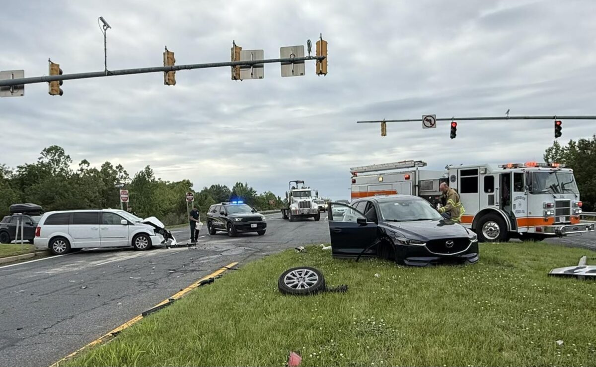 Two cars are wrecked at a rainy intersection while police, fire, and an ambulance respond.