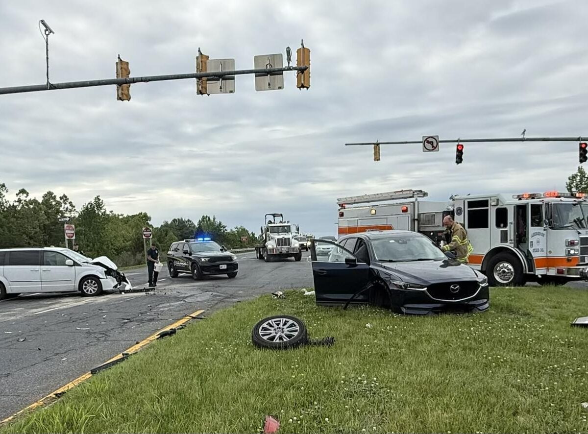 Two cars are wrecked at a rainy intersection while police, fire, and an ambulance respond.