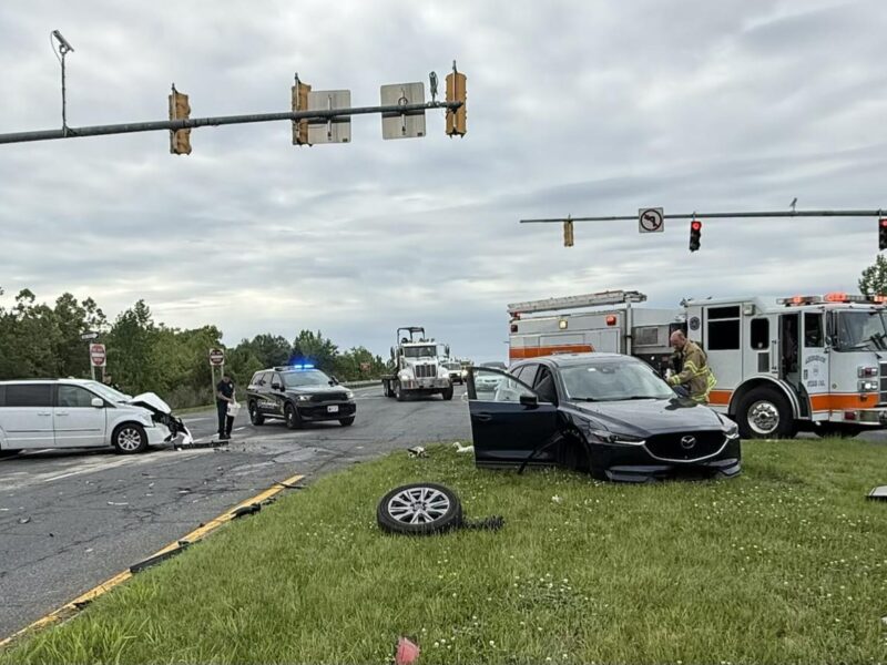 Two cars are wrecked at a rainy intersection while police, fire, and an ambulance respond.