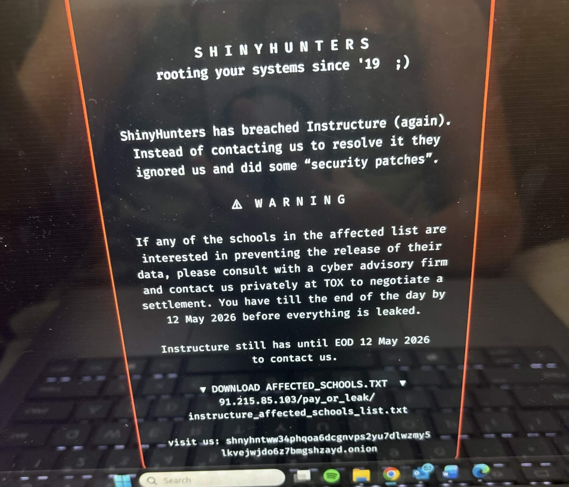 Laptop screen showing a black warning page from ShinyHunters about a security breach and leaked school data.