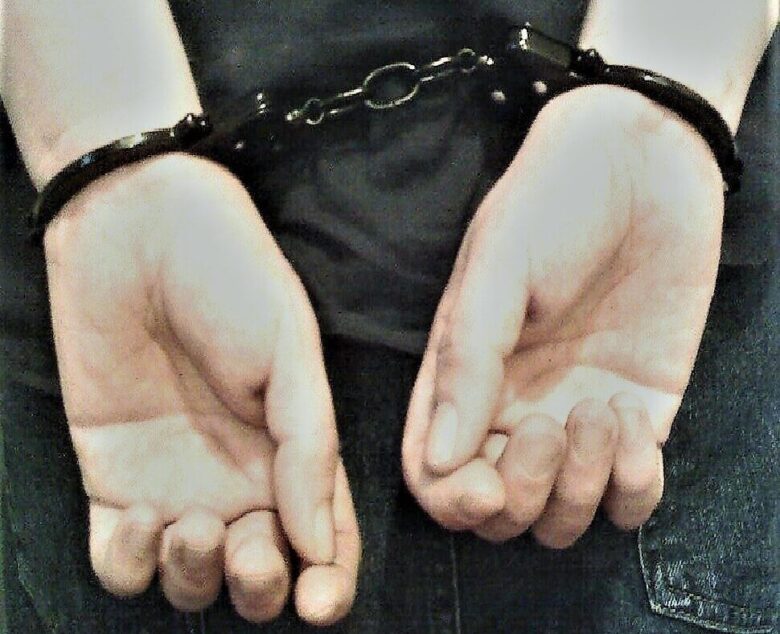Handcuffed hands held behind the back in a dark, close-up scene.