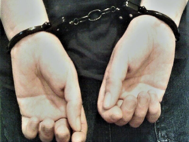 Handcuffed hands held behind the back in a dark, close-up scene.