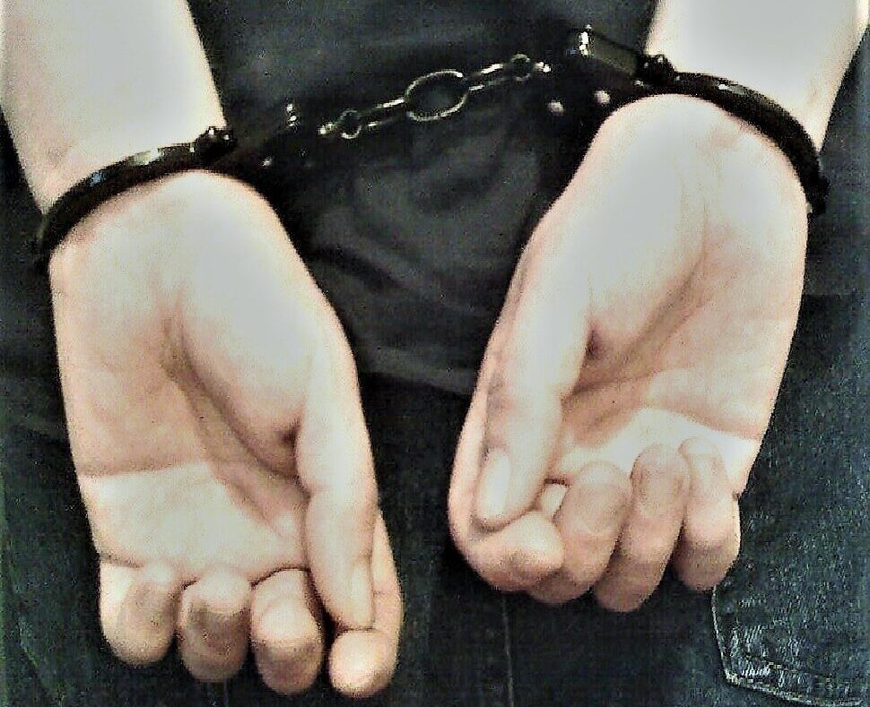 Handcuffed hands held behind the back in a dark, close-up scene.