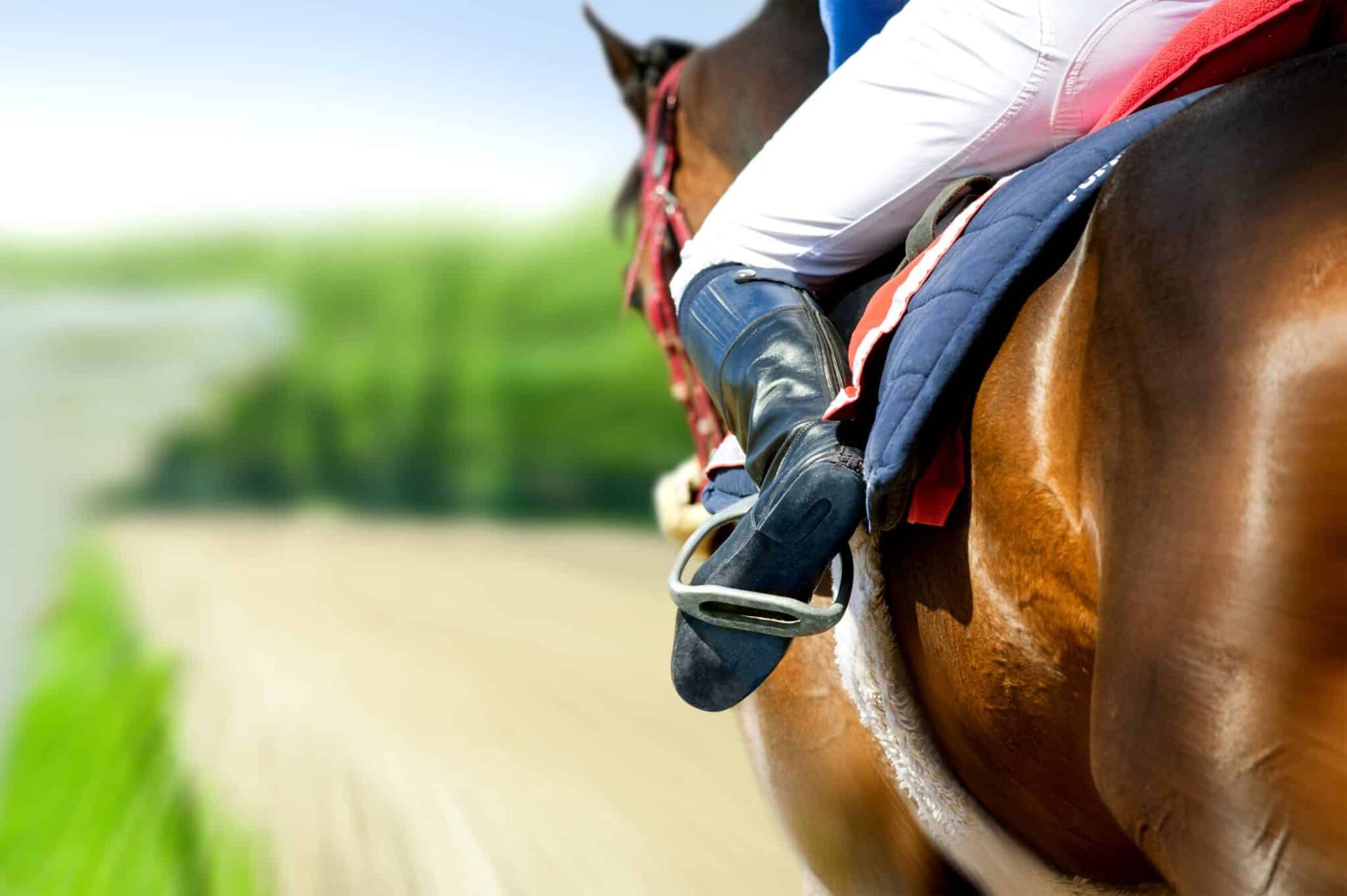Rider in white pants and black boots on a brown horse galloping along a dirt track.