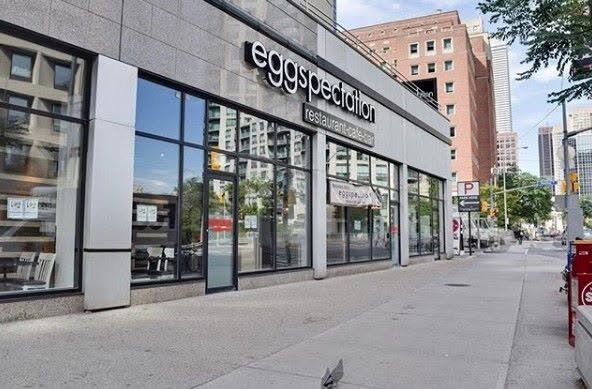 Modern storefront of Eggspectation restaurant on a city street with glass windows and sidewalk.