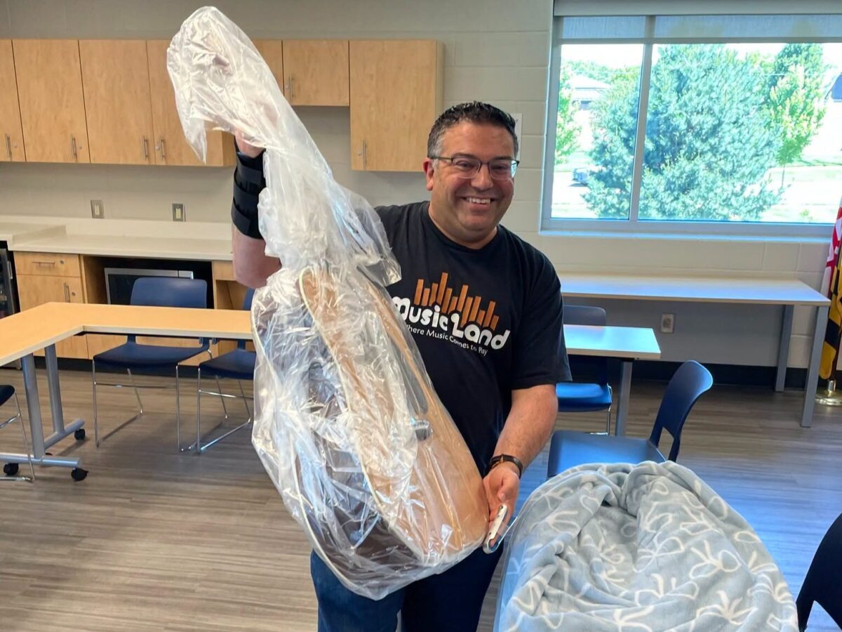 Smiling man holding up a long wrapped object in a classroom or workshop setting.