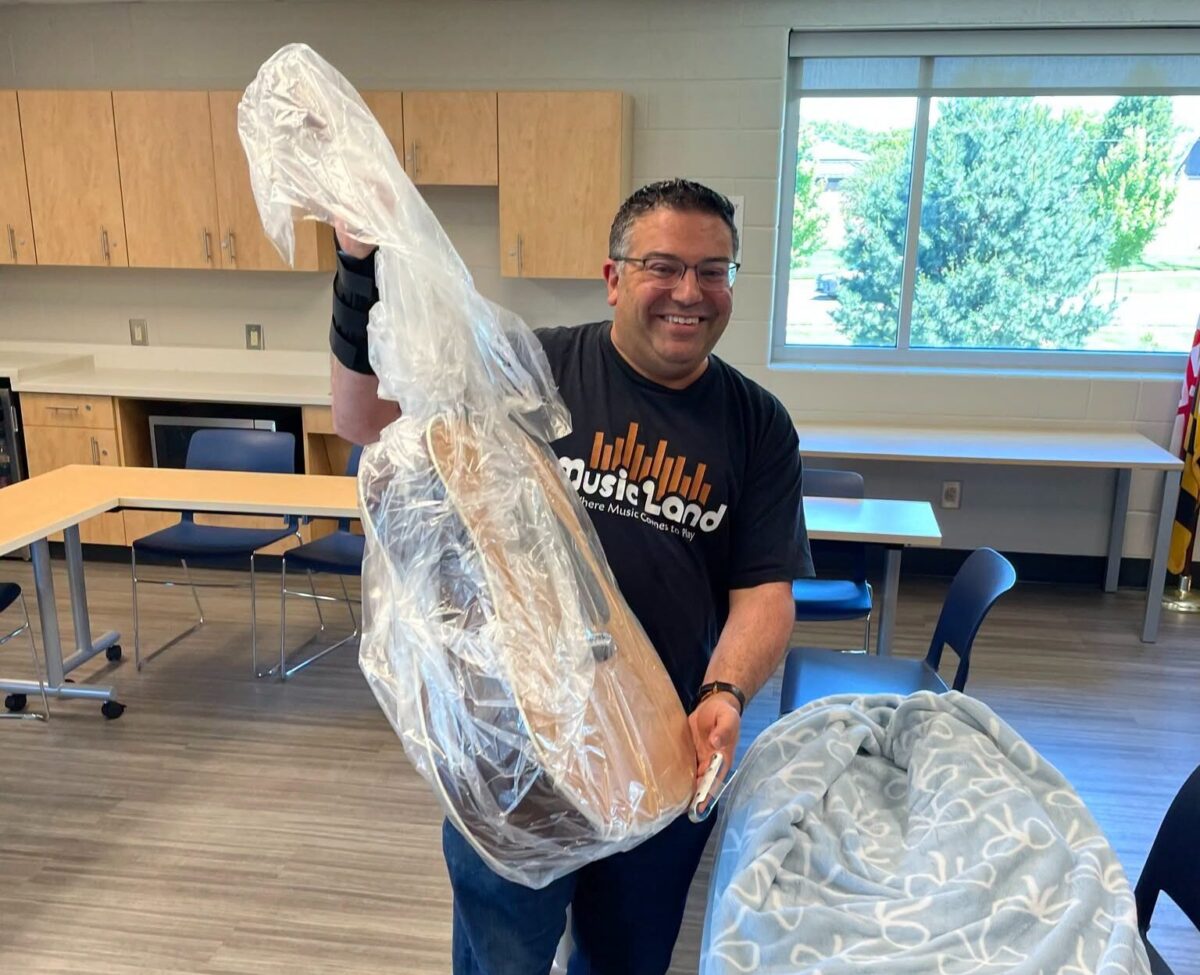 Smiling man holding up a long wrapped object in a classroom or workshop setting.