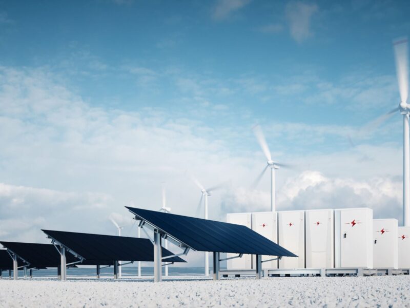 Solar panels and wind turbines beside battery storage units under a blue sky.