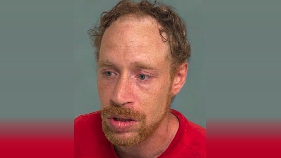 Close-up of a red-haired man in a red shirt against a gray background.