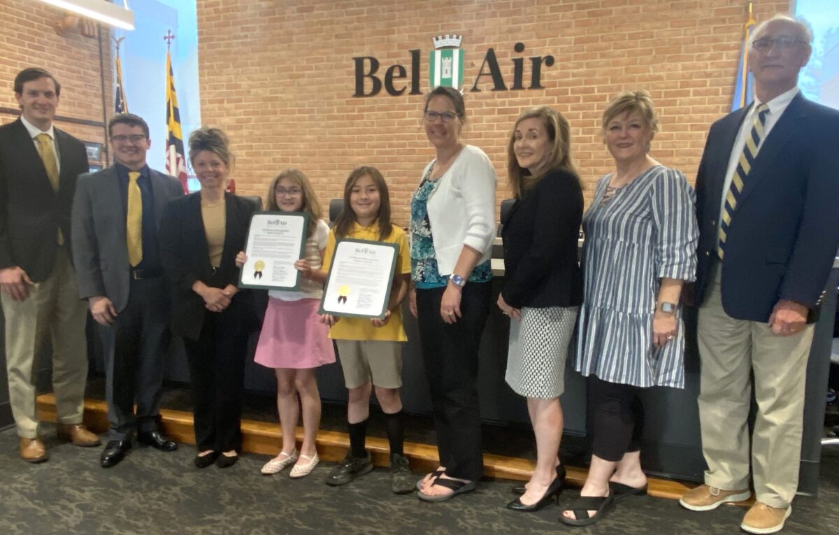 Group of adults and two girls posing with certificates in a Bell Air lobby.