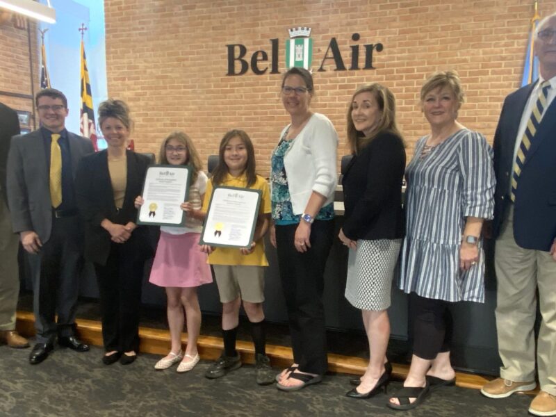 Group of adults and two girls posing with certificates in a Bell Air lobby.