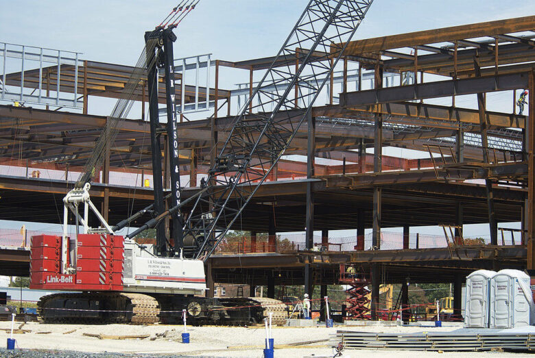 Crane lifts steel beams at a multi-story building construction site.