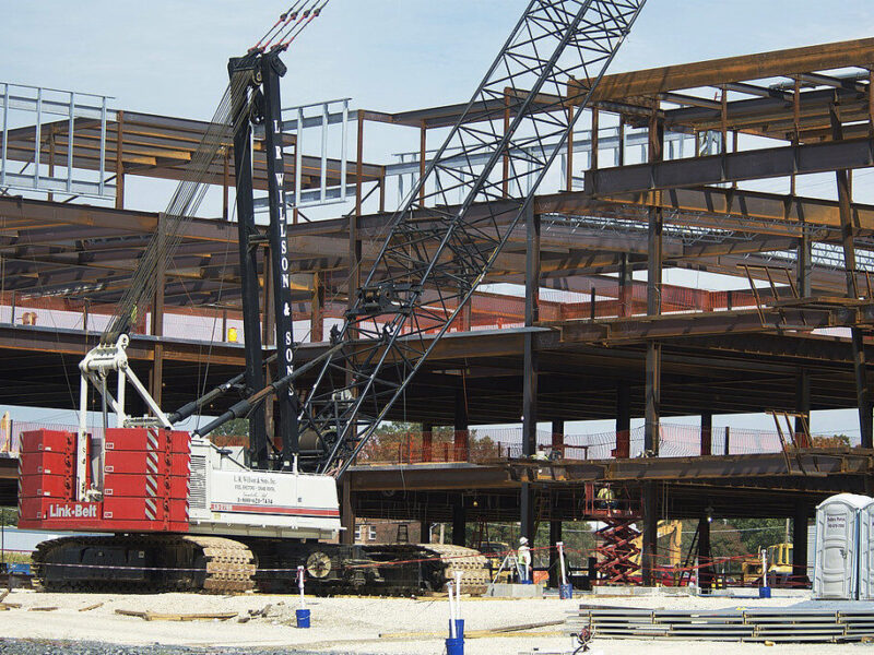 Crane lifts steel beams at a multi-story building construction site.