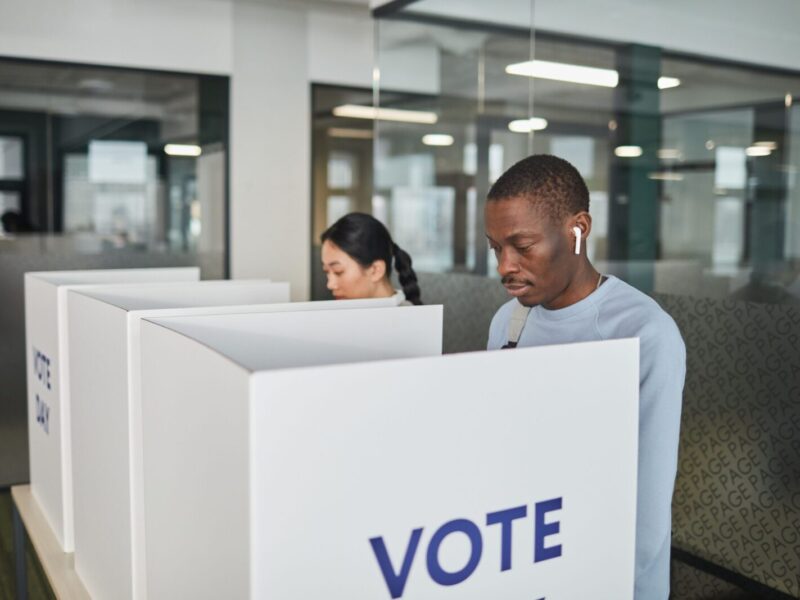 Two individuals casting votes in an indoor voting booth, emphasizing democracy.