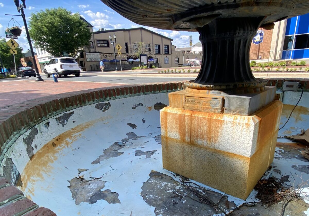 Empty, peeling fountain basin with a central pedestal in a sunny downtown square.
