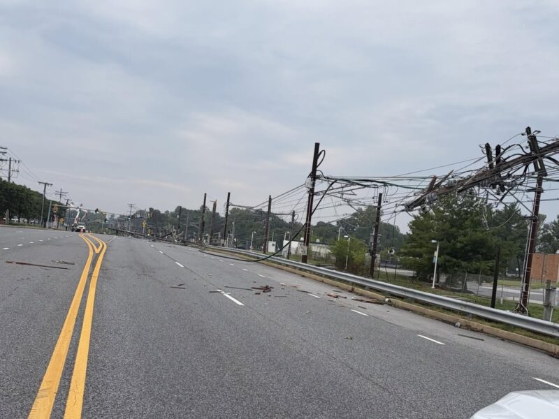 Empty suburban road with downed power lines and debris after a storm.