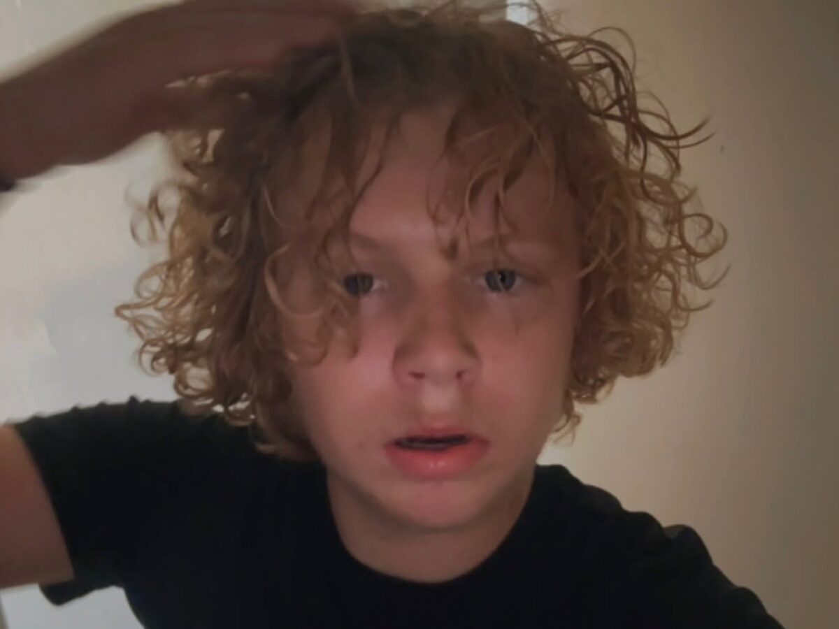 Curly-haired person in a black shirt touching their hair indoors.