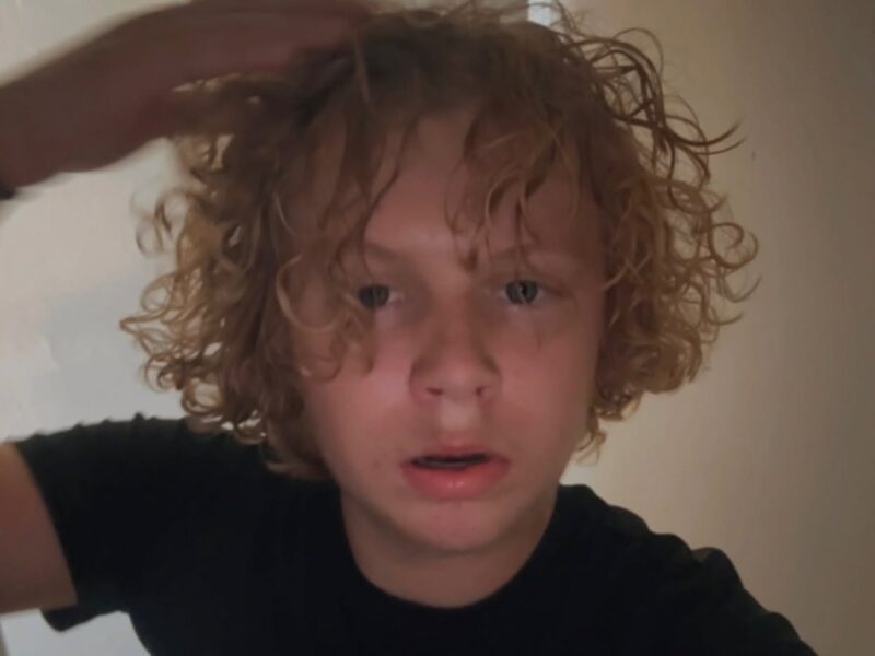 Curly-haired person in a black shirt touching their hair indoors.