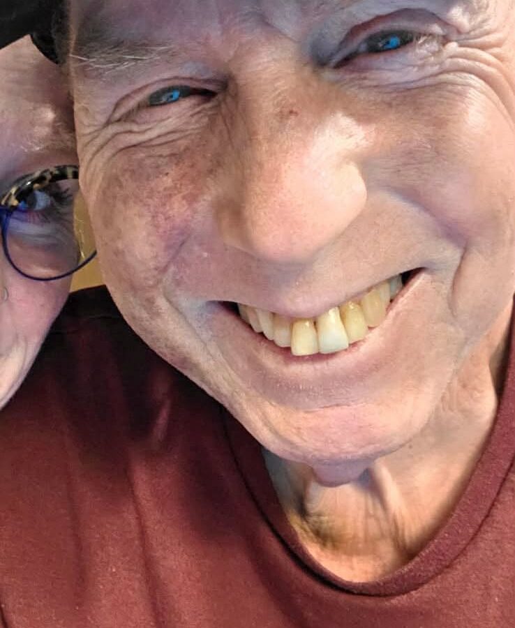 Close-up of a smiling man wearing a cap and maroon shirt.