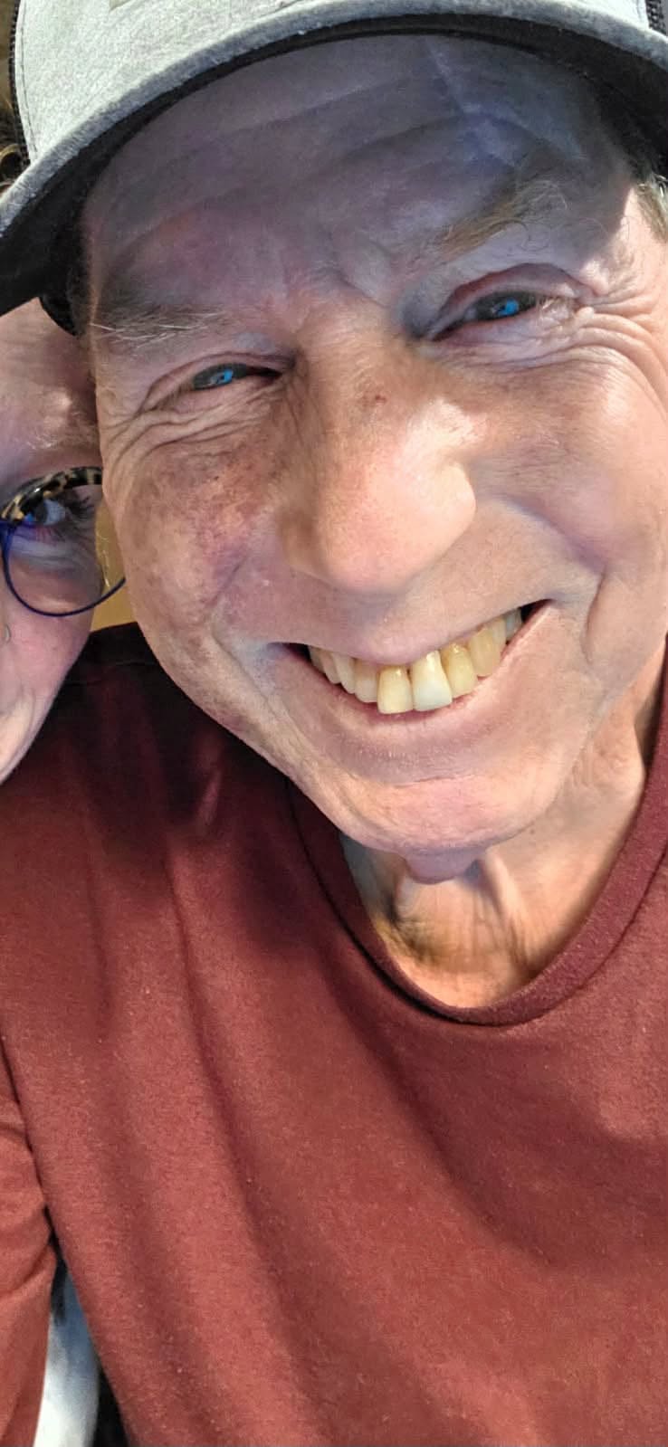 Close-up of a smiling man wearing a cap and maroon shirt.