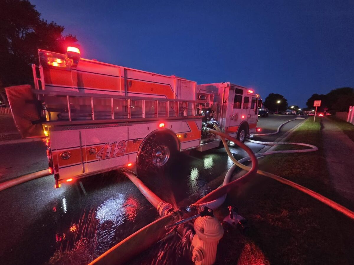 Fire truck at night with hoses laid across a wet street and red emergency lights flashing.