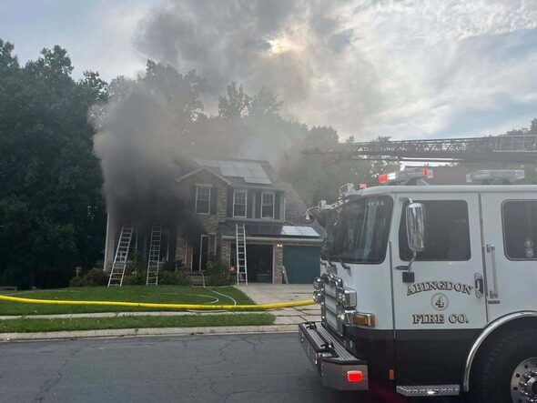 Fire truck in front of a smoke-filled house with ladder and yellow hose during a firefighting response