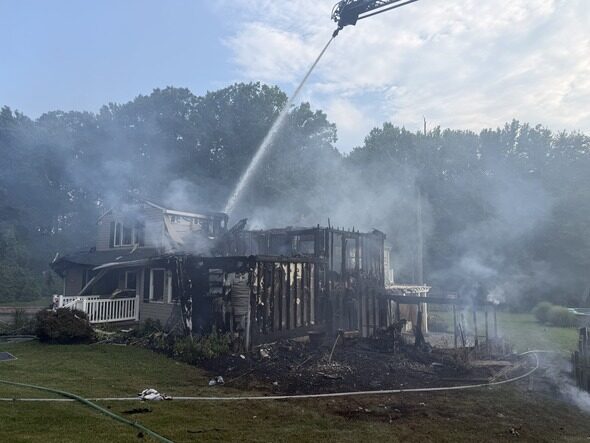 Firefighters douse a burned house with heavy smoke rising from the charred remains.