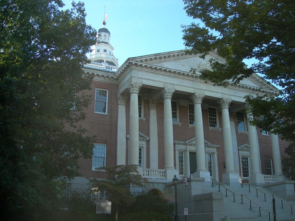 Historic brick courthouse with tall white columns and steps, partly framed by trees.