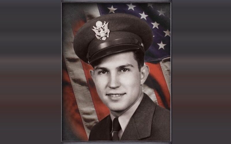 Portrait of a young man in a military uniform before an American flag backdrop.