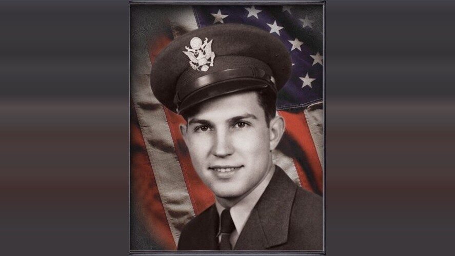 Portrait of a young man in a military uniform before an American flag backdrop.
