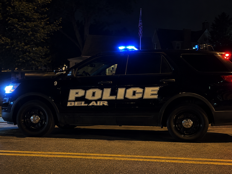 Belair police SUV with flashing blue lights parked on a dark street at night.